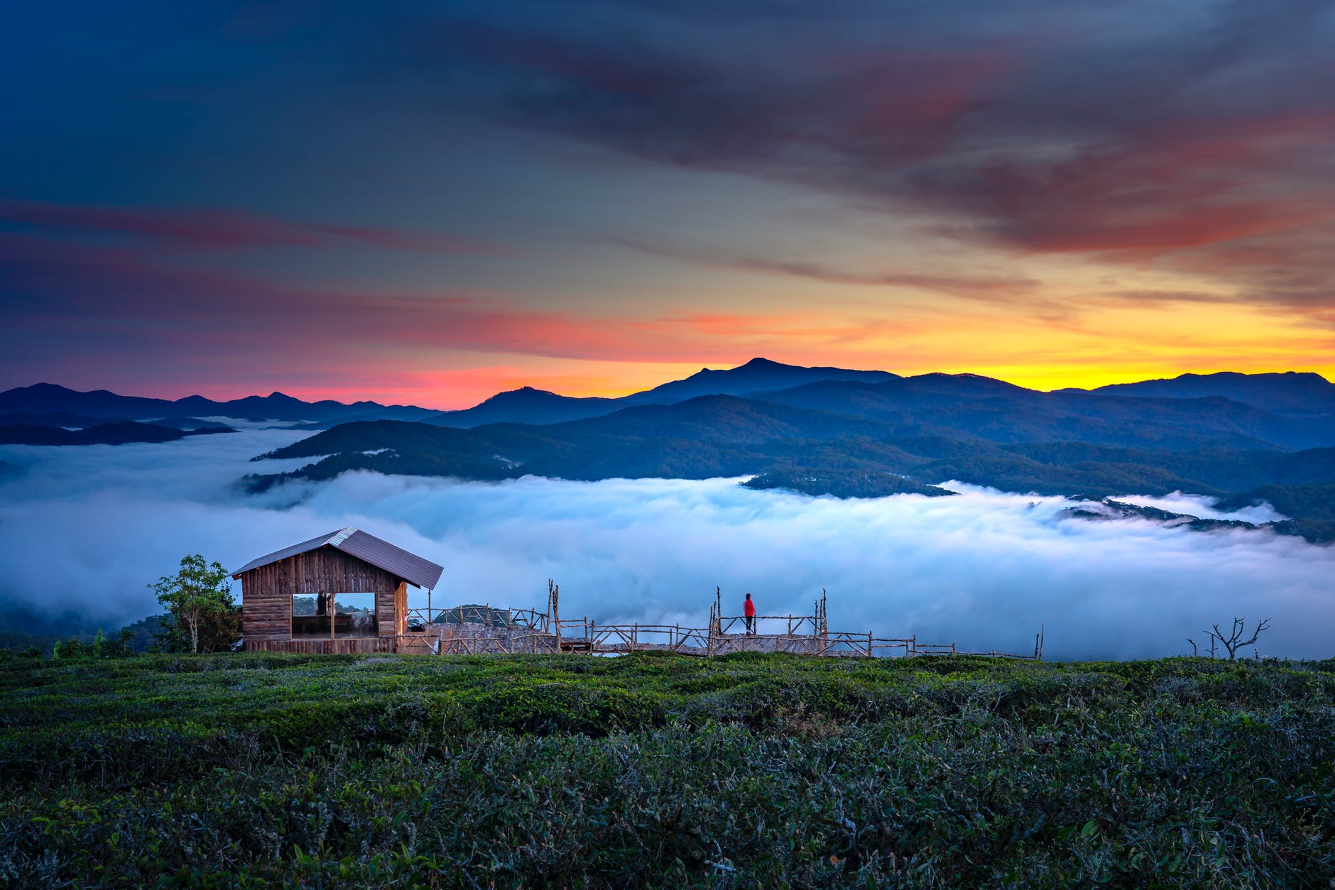 brown wooden house near green field and mountain view under orange and yellow skies